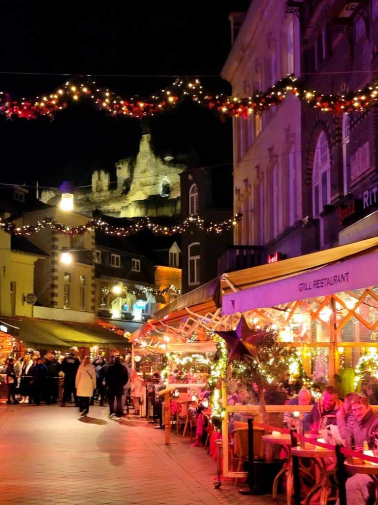 A castle ruin on a hill illuminated and an outdoor cafe at night wtih christmas lights