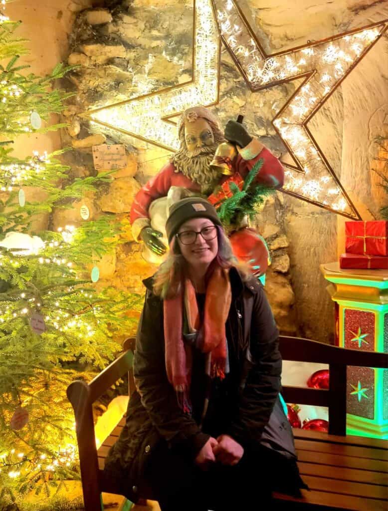 A woman sitting on a bench in a limestone cave next to a christmas tree with Santa and a large star behind