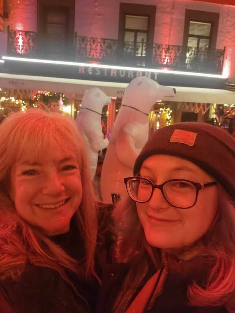 Two women bathed in red light with polar bears marching in the Valkenburg Christmas market parade behind