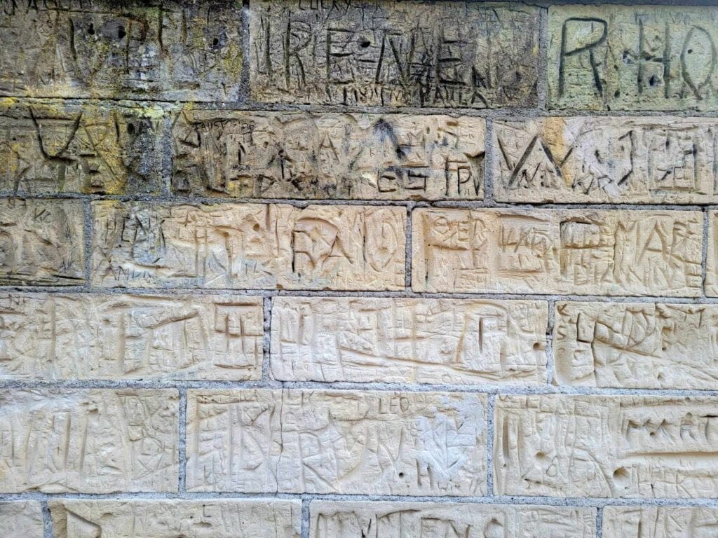 A wall made of limestone blocks with many carvings of initials and symbols