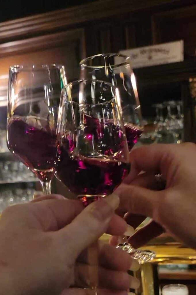 Three people toasting with small wine glasses filled with purplish liqueur