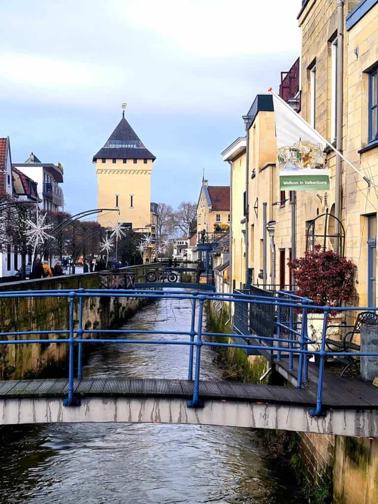 A bridge over a canal with yellow buildings on the side and a tower in the background