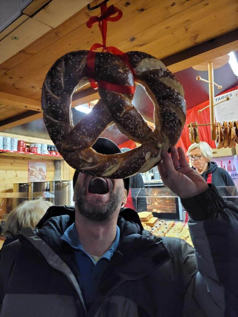 A man pretends to eat a giant hanging pretzel at the front of a market stall