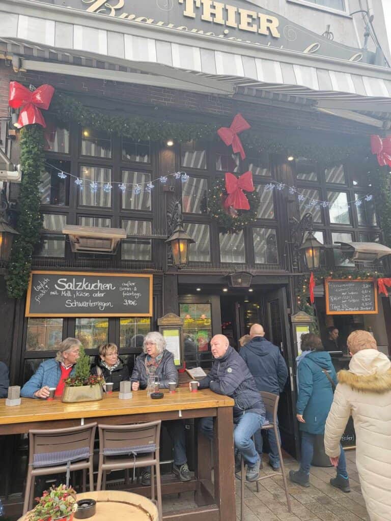 People sitting at an outside table by an old looking pub drinking beer