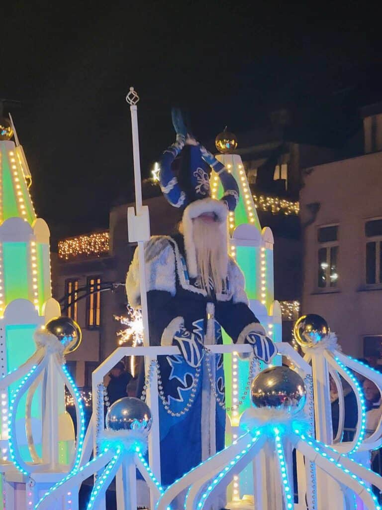 Sinterklass in a blue outfit with white fur and a long white beard riding on a blue and white float