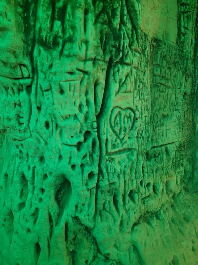 A green light bathing a limestone wall carved with initials