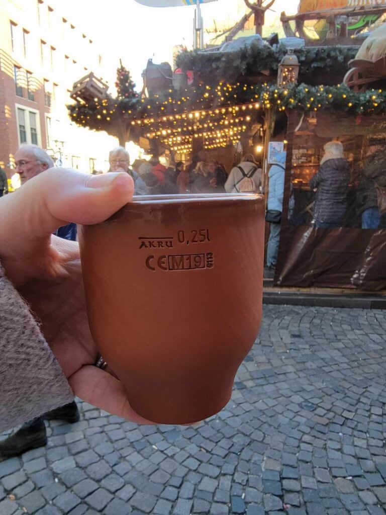 A woman's hand holding a fired clay mug with steaming wine