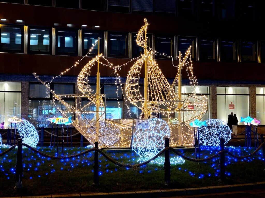 A large old time sailing ship made of gold lights on an ocean of blue lights