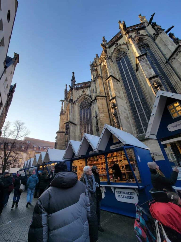 A row of market stalls with pointed roofs underneath St. Lambert's gothic church