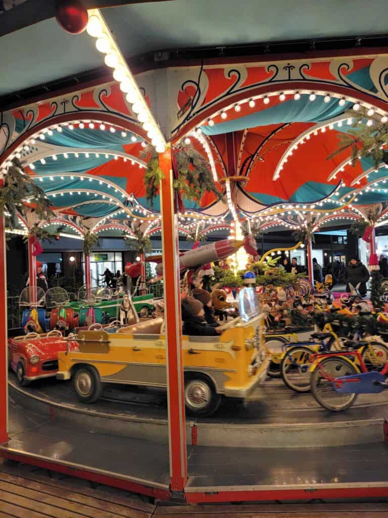 An antique carousel with a yellow gruck, a red car, and bicycles to ride