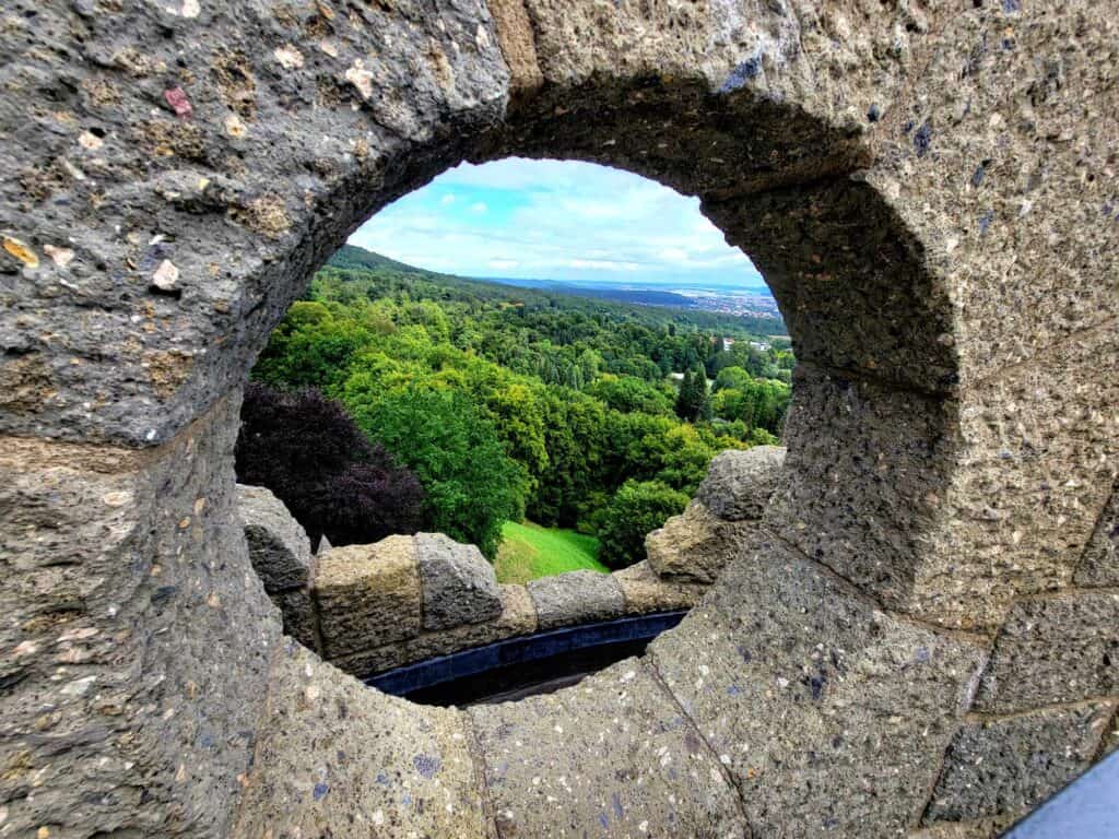 A view of trees and hills through a round stone viewing portal