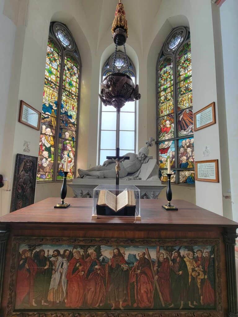 An altar with an old Bible under lucite, stained glass windows behind