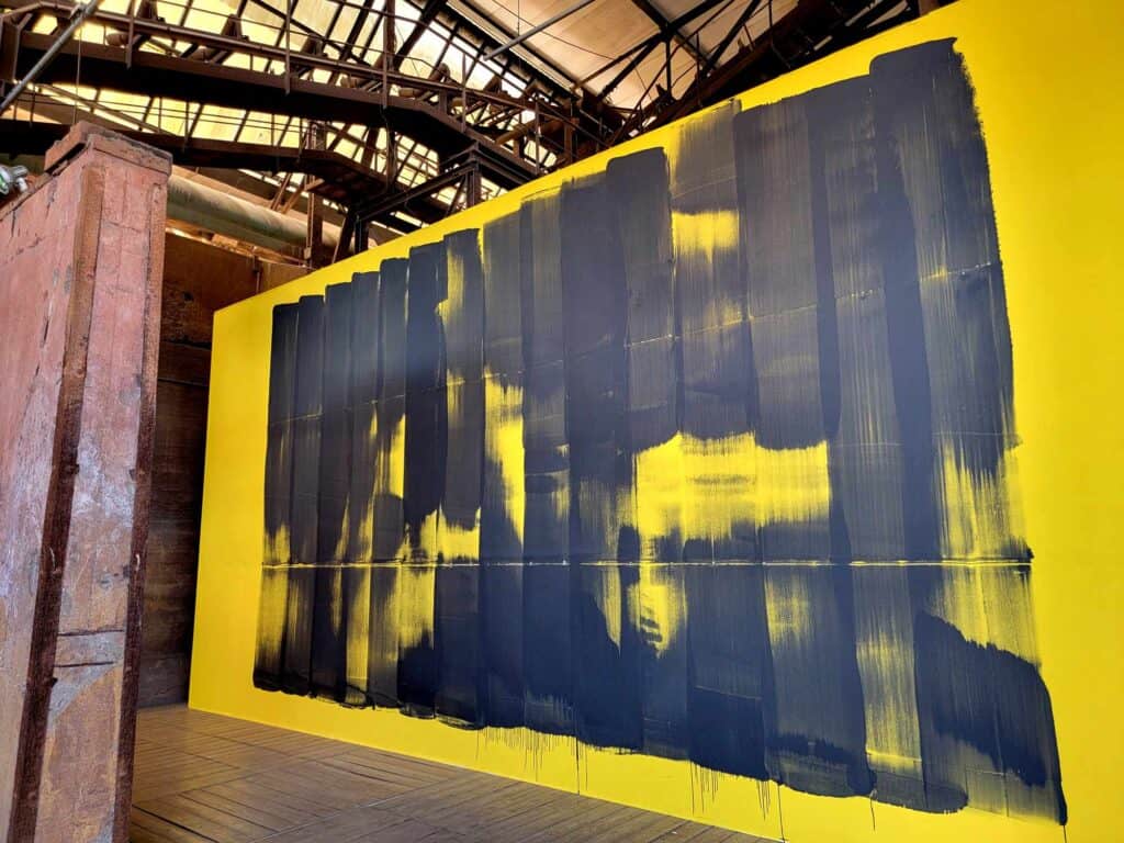 A contemporary artwork of black paint strokes on a yellow background