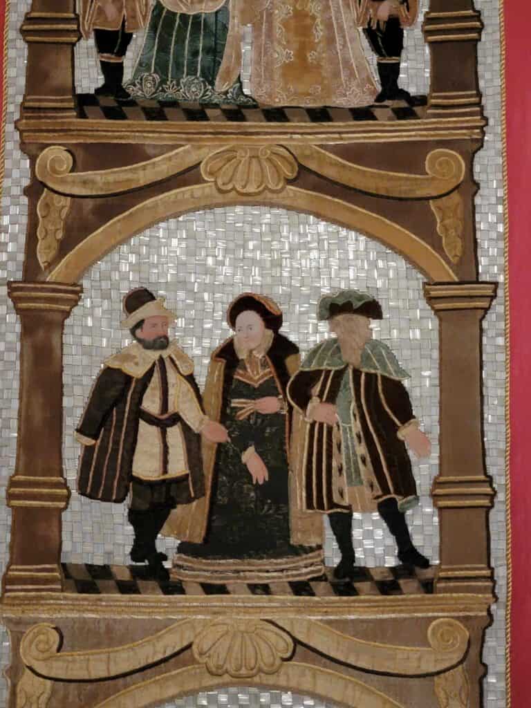 Detail of a wall covering showing two men and a woman in long cloaks with a beaded glass background