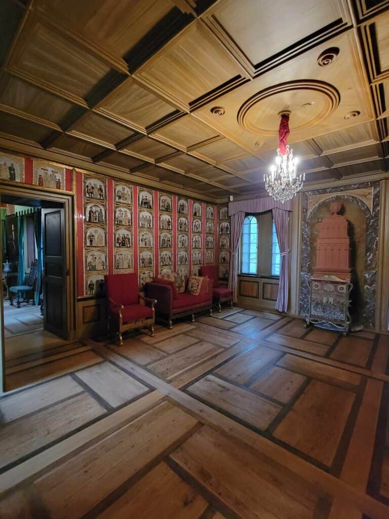 A room with an inlaid wooden floor and red velvet chairs with wall coverings