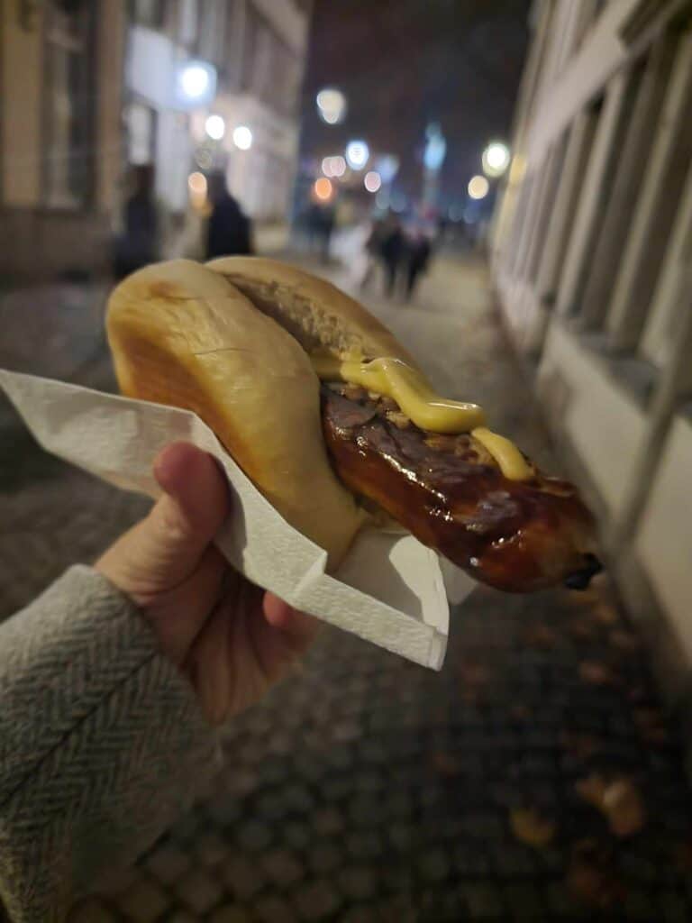 A hand holding a bratwurst with mustard