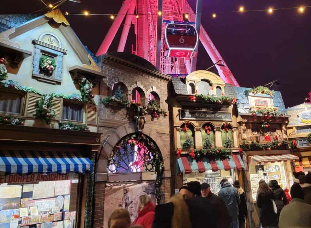 Elaborate Christmas market stalls that look like old buildings and a ferris wheel behind