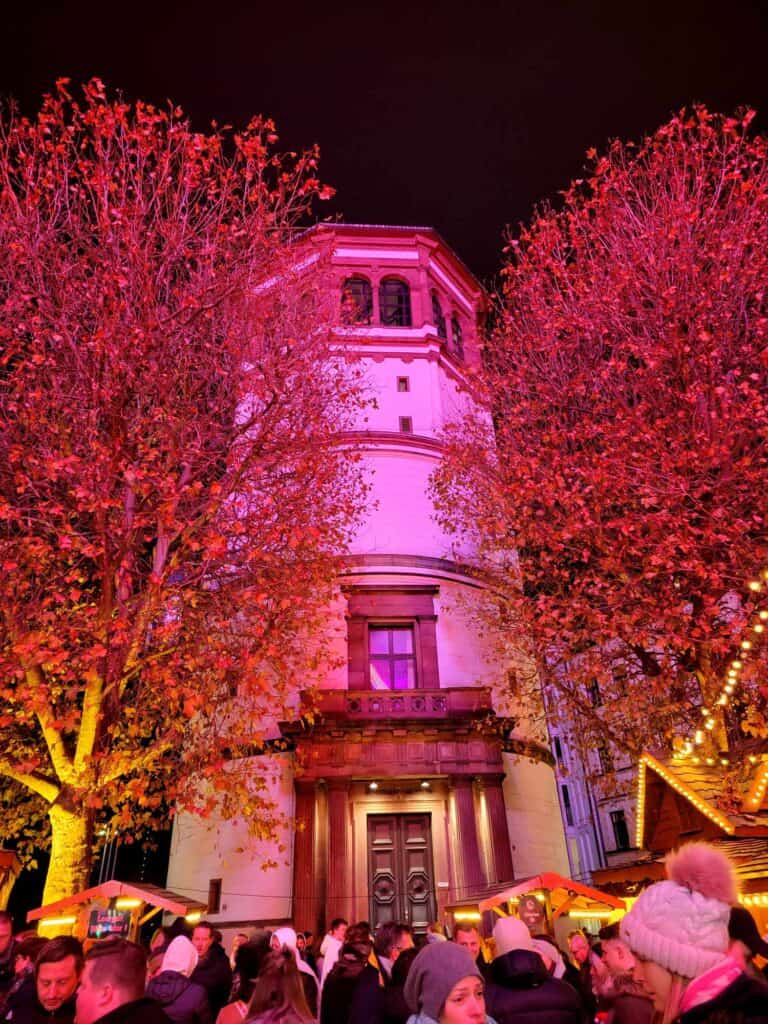 A white tower in the medieval style flooded in pink light with two trees on either side