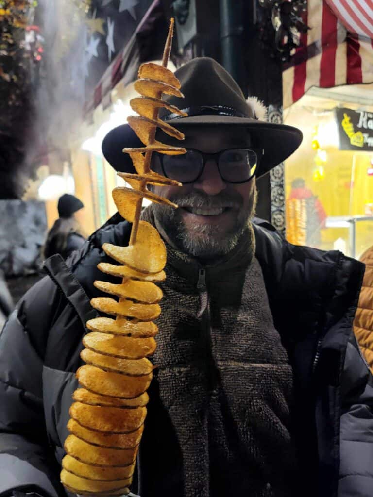 A smiling man in a hat with a potato tornado on a stick