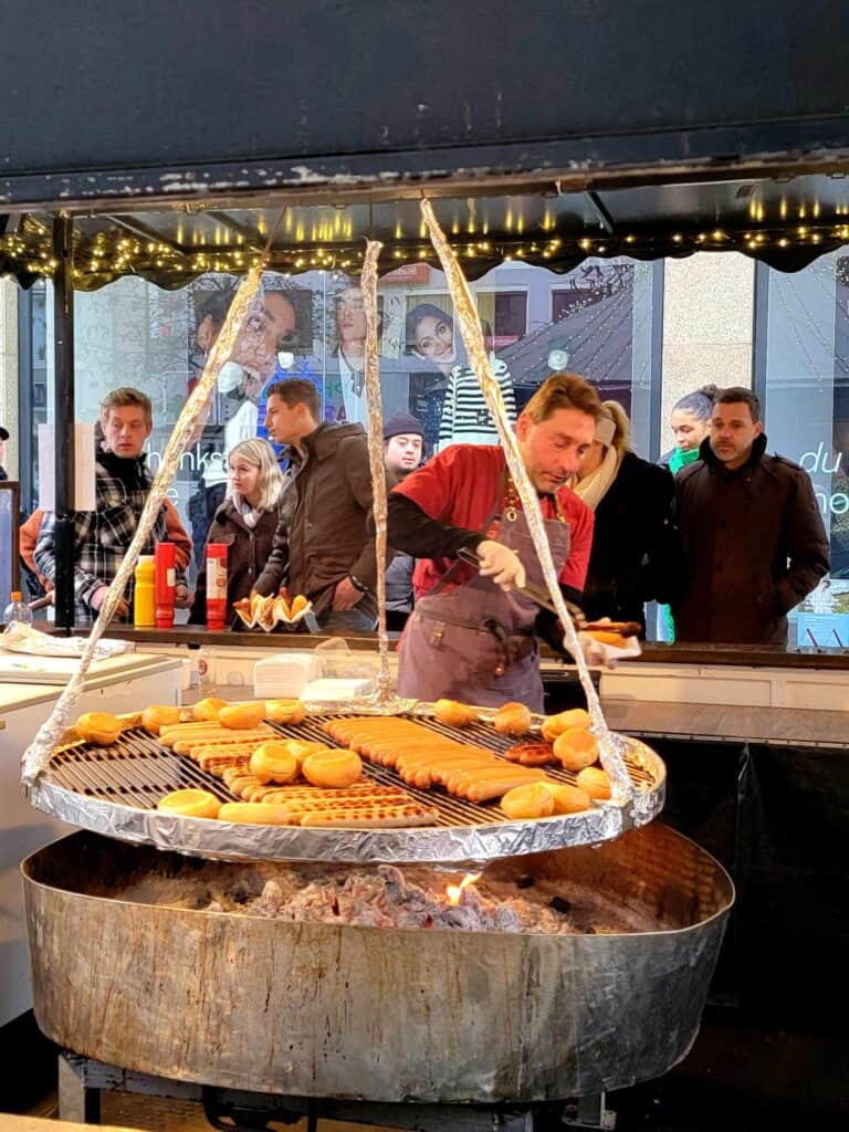 A man grilling a bunch of sausages on a large round grill over coals