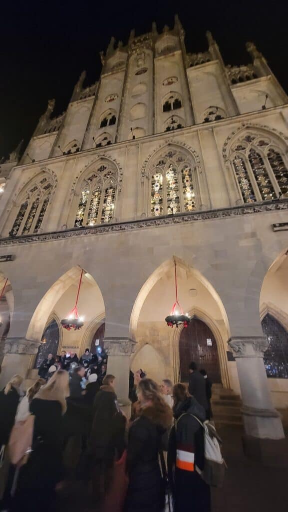 A white stone building with multiple tiers and pointed gothic arches, some with stained glass windows