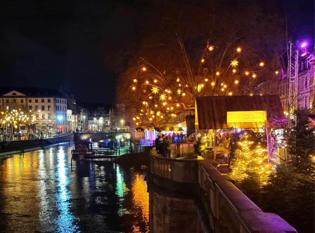 A river with a party boat and a crowd of people underneath a tree with hanging stars