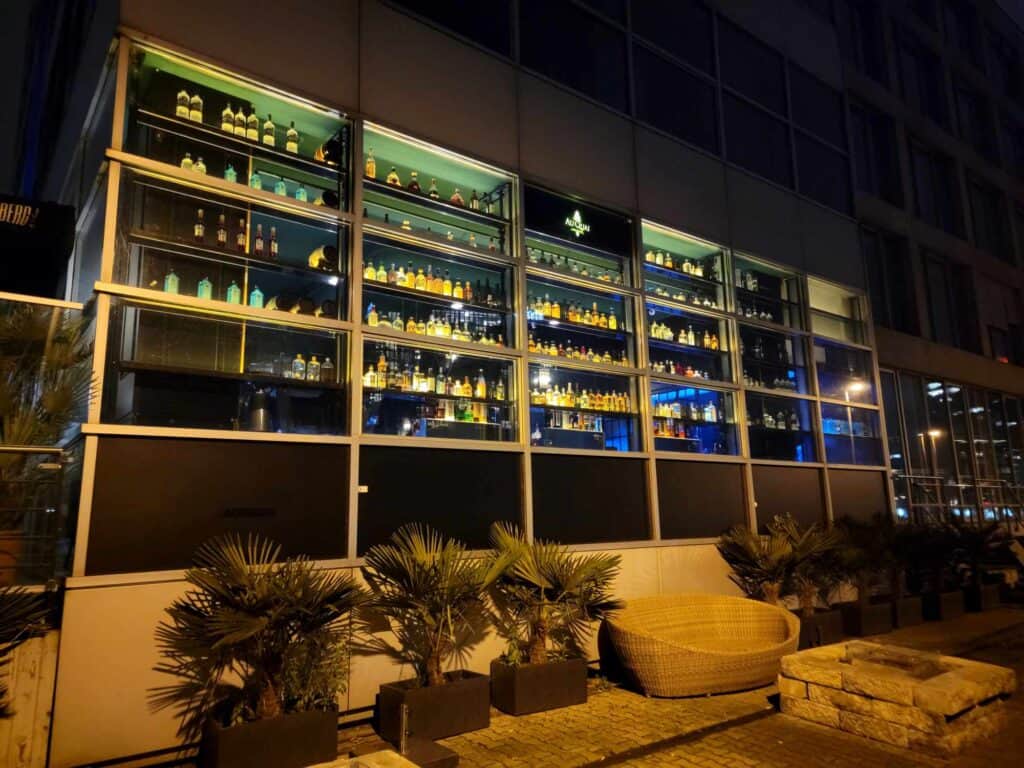 A glass wall illuminated from within and shelves filled with liquor bottles