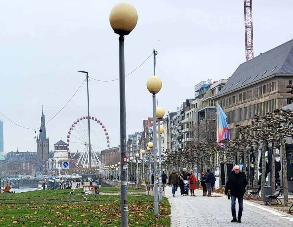 A walkway with globular street lights and a ferris wheel behind