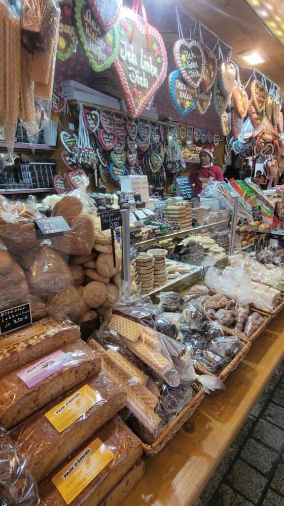 A woman in a Santa hat behind the counter at a stand selling all kinds of sweet baked goods