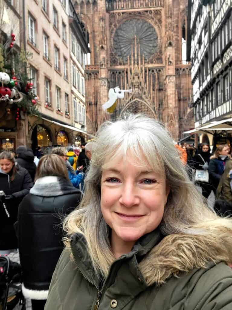 A smiling woman in front of the facade of Strasbourg cathedral