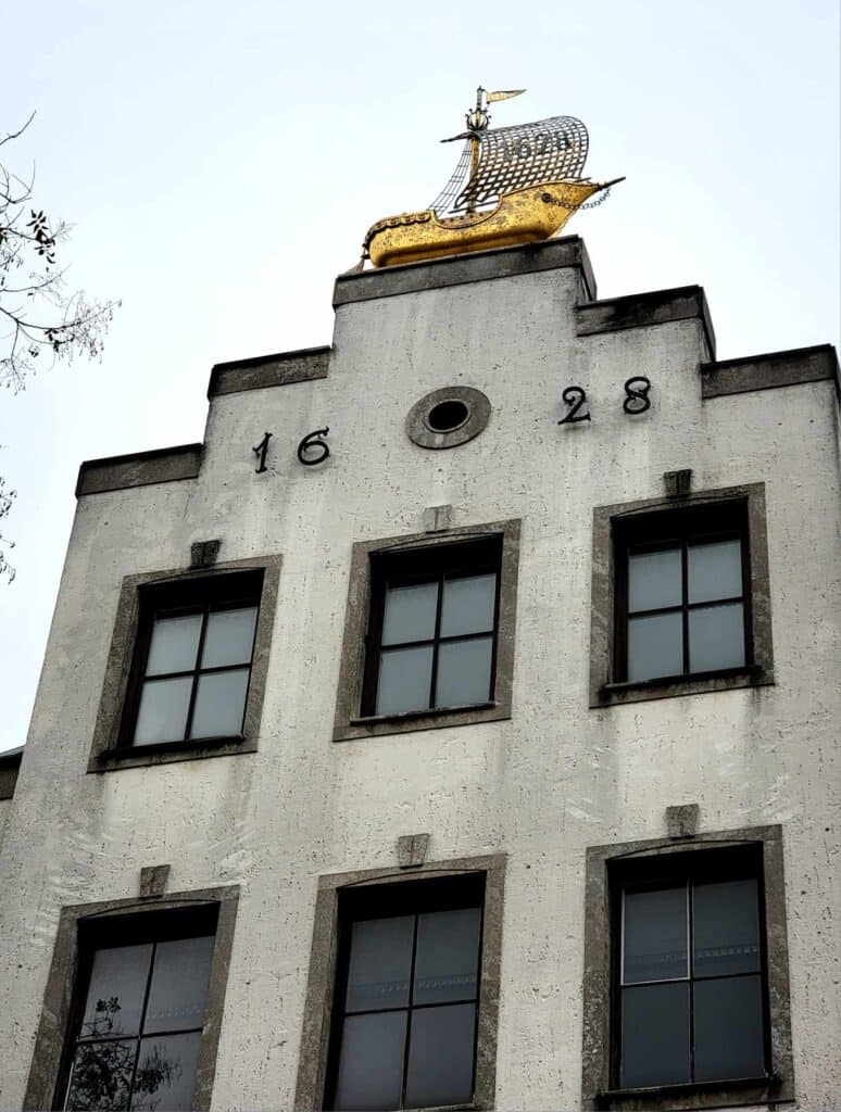 A stepped white facade of a building with 1628 on it and a gold sailing ship on the peak