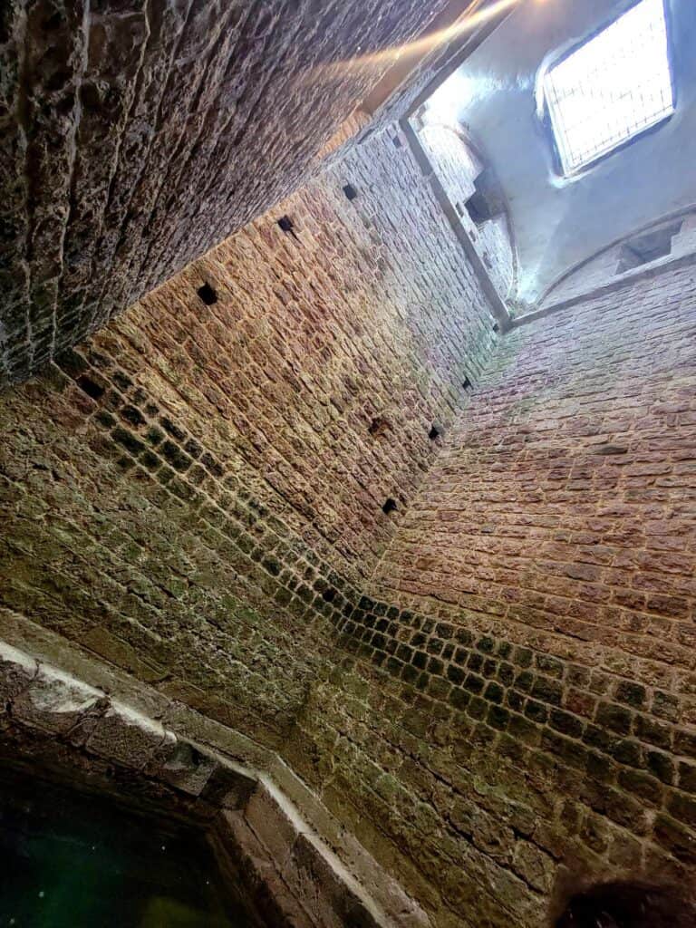 A mikvah at the bottom of a tall bricked room with a skylight on top