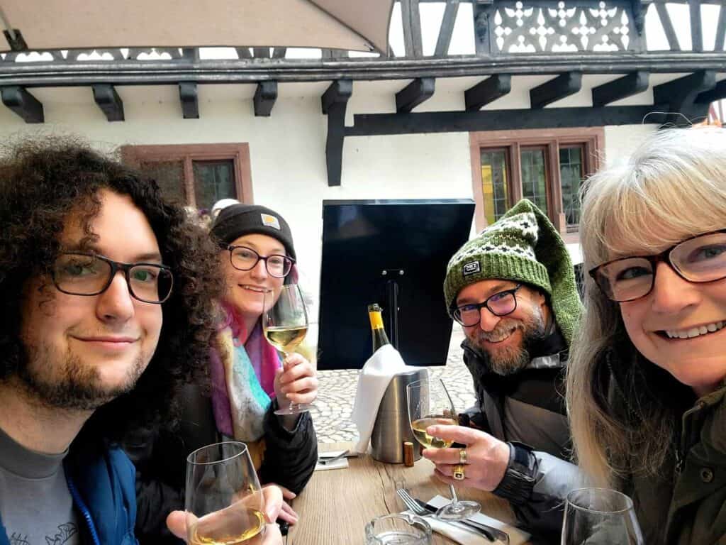 Four smiling people toasting with glasses of white wine at a table outdoors