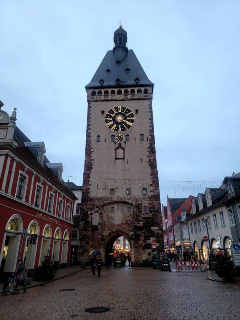 A tall squared tower with a clock face and a pointed arch at the bottom