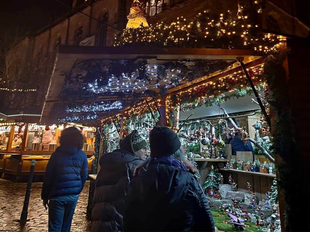 People shopping at a stall lit up with tiny lights and full of Christmas ornaments