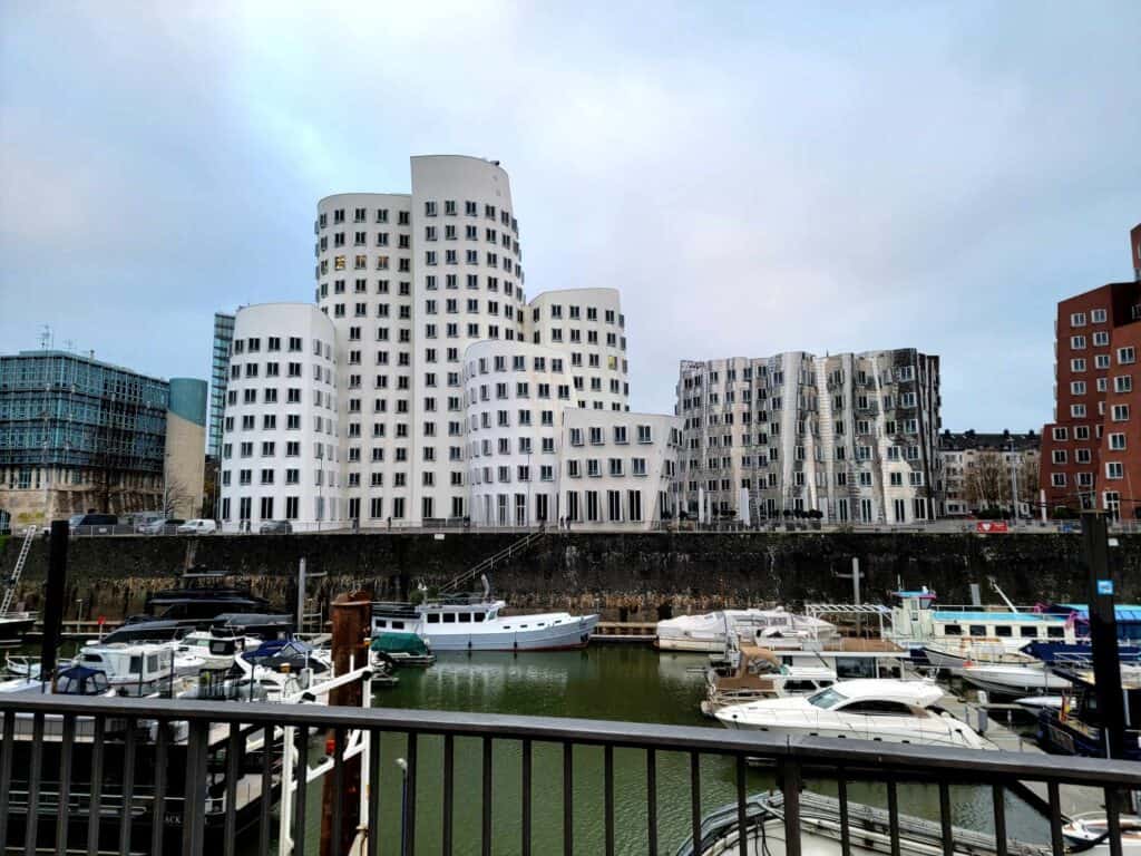 White buildings with rows of square windows that are curved and look like they're made of jello. A harbor in front