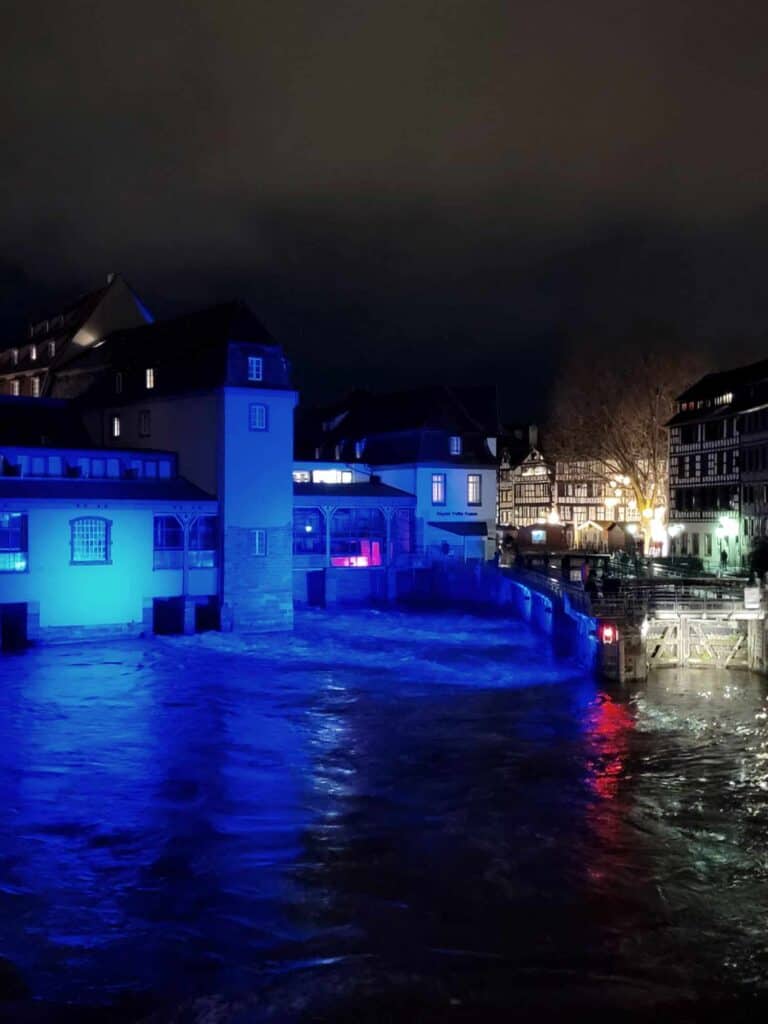 A tower and buildings lit in blue reflected in a river