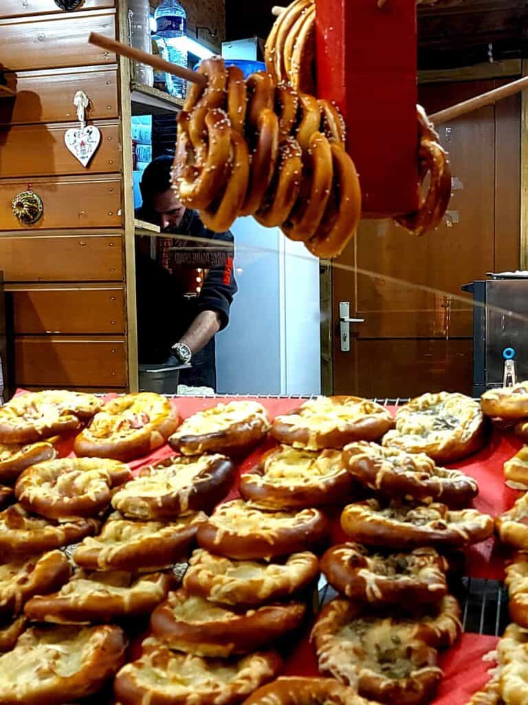 Salted pretzels hanging on a peg over a spread of pretzels with melted cheese