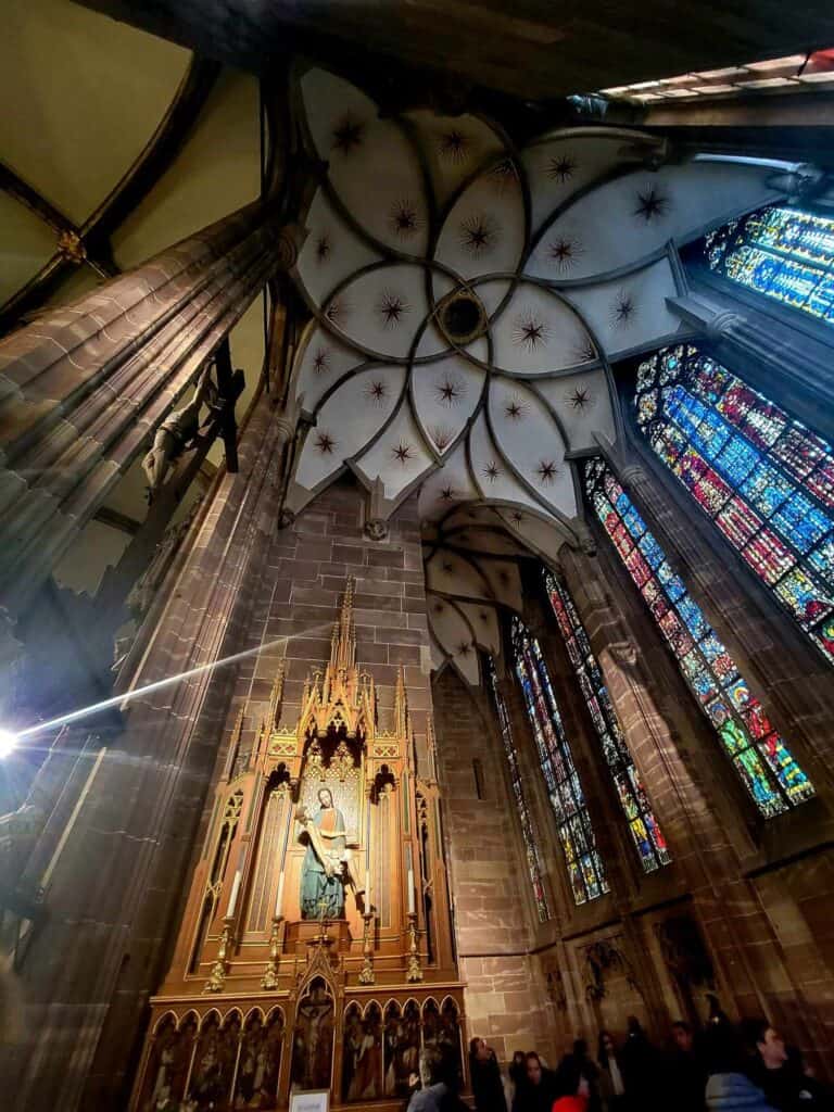 A wooden statue of Mary and Jesus, stained glass and a vaulted ceiling in white with stars