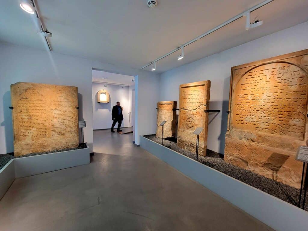 A man walks through a museum room featuring old jewish tombstones and inscriptions in sandstone