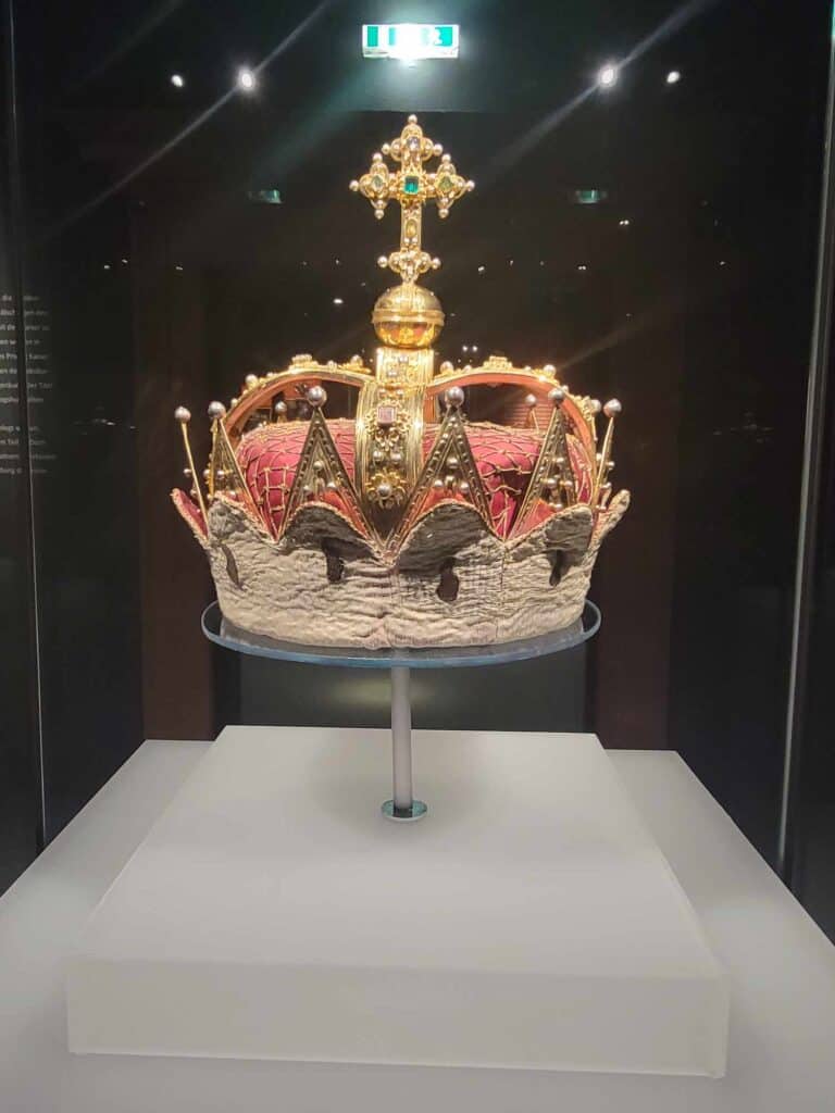 A golden crown with red and white fabric and a golden cross with an emerald