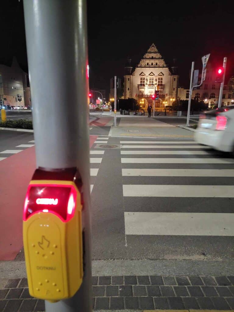 A yellow plastic hand signal box illuminated on a utility pole and a crosswalk to the right