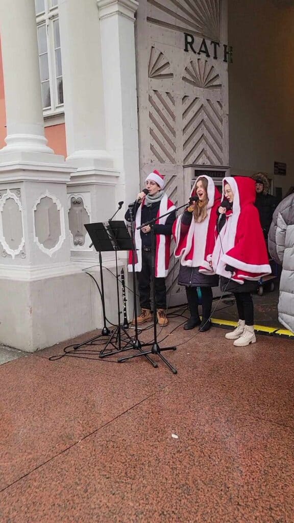 Three women in red Santa capes singing at a microphone