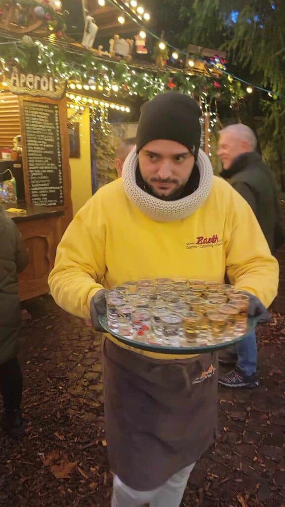 A man carries a tray with a couple dozen shot glasses full of schnaps