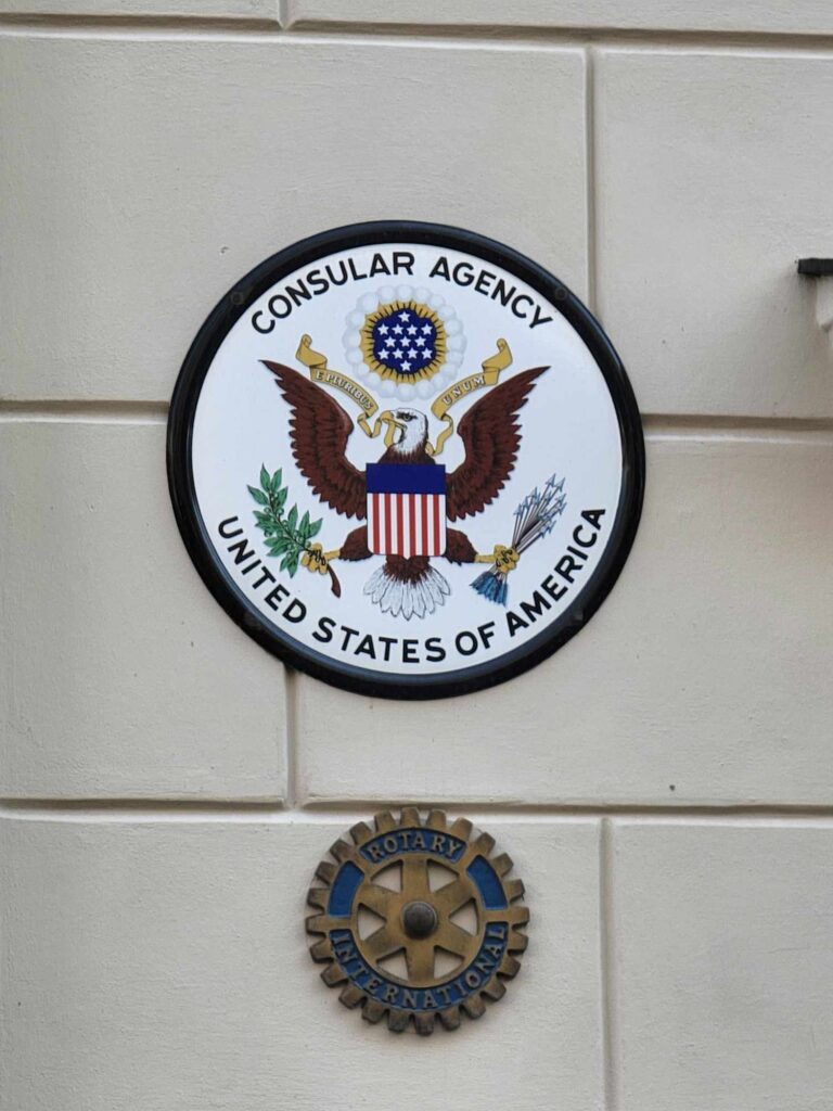 A round plaque showing the American eagle as seen on the US dollar. Text reads Consular Agency United States of America. A small insignia below says Rotary International