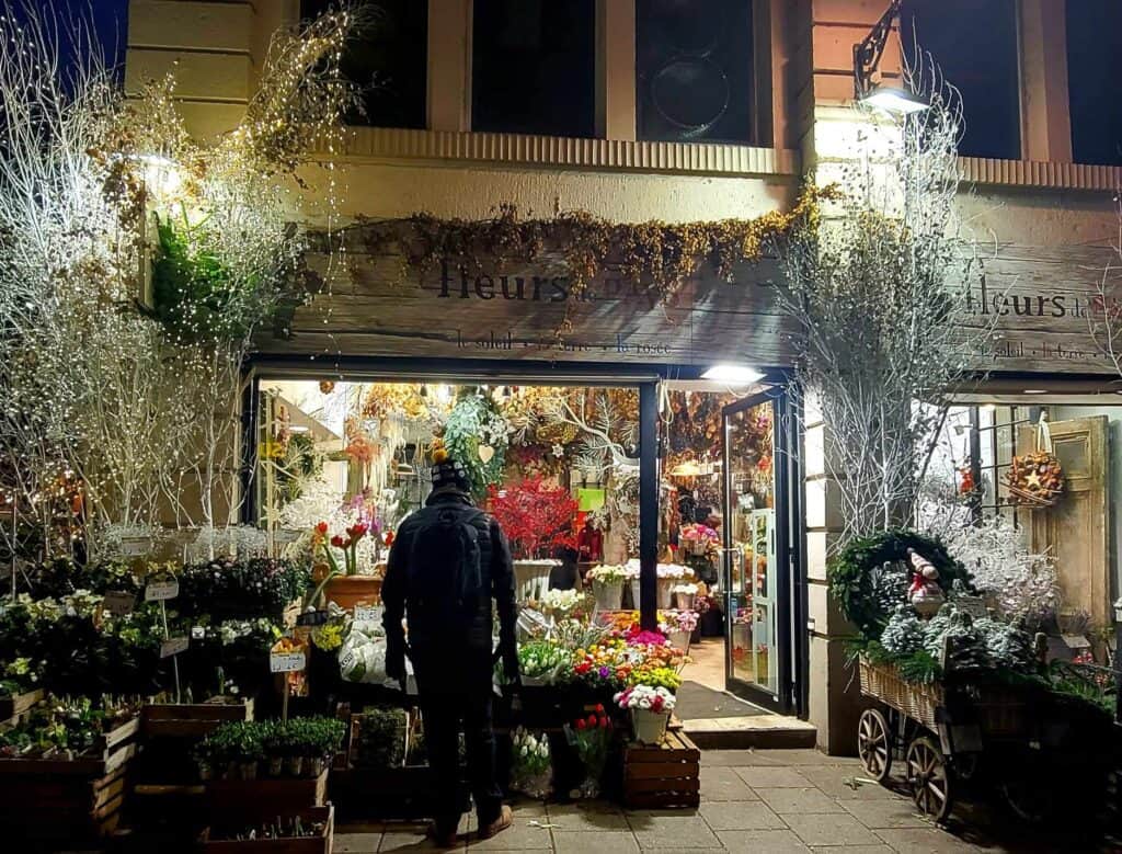 A man stands in front of a florist shop filled with plants and flowers with a mistletoe garland over the canopy