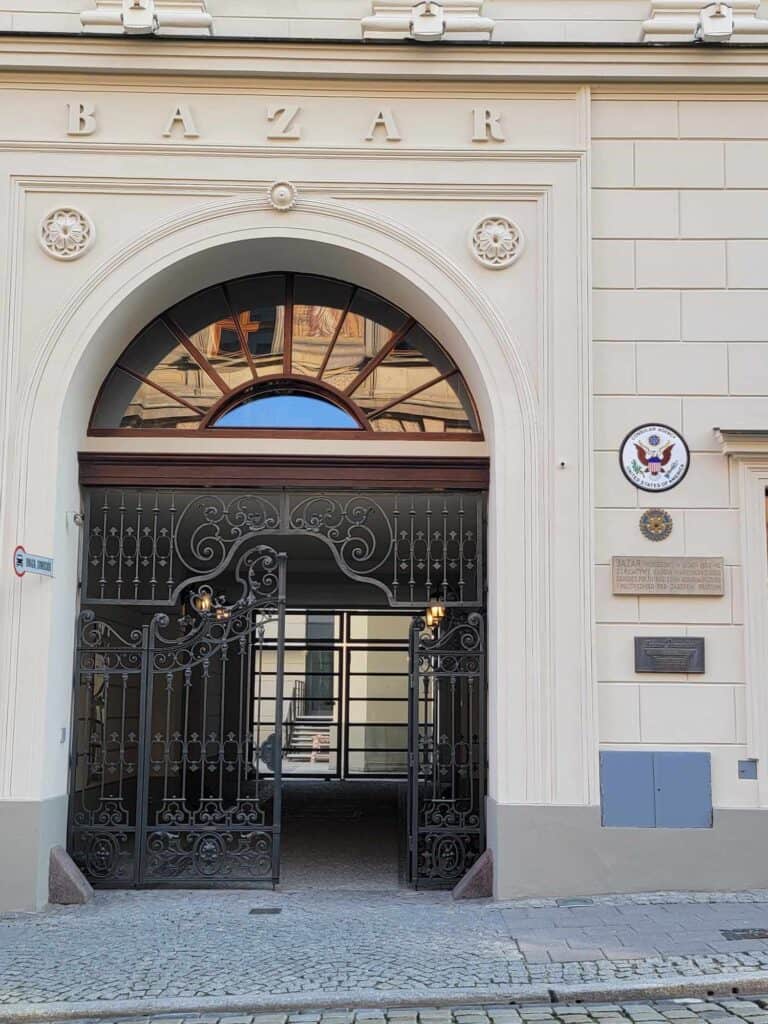 A white stone building with an arched doorway covered by a wrought iron gate and a round plaque with an American eagle