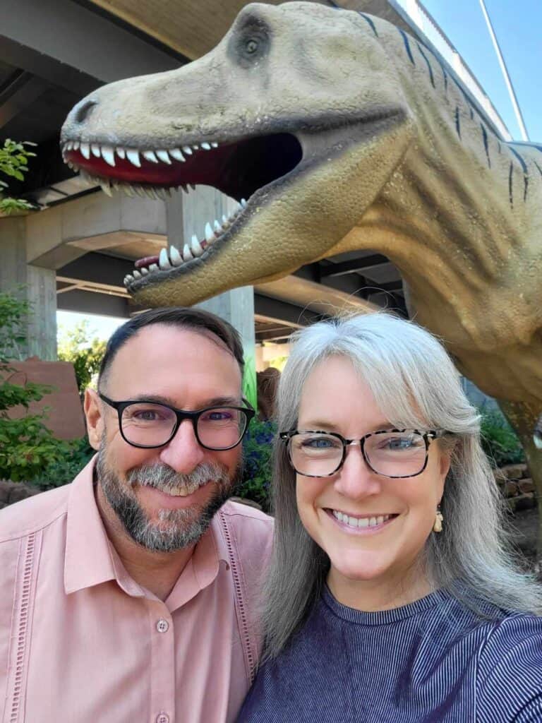 A smiling couple in front of a T-Rex baring its teeth