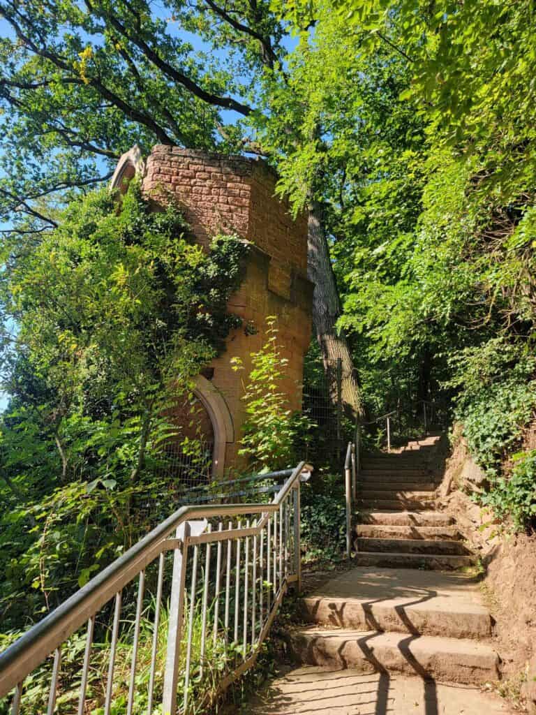 Red sandstone stairs and a sturdy metal railing lead up past a gothic style tower