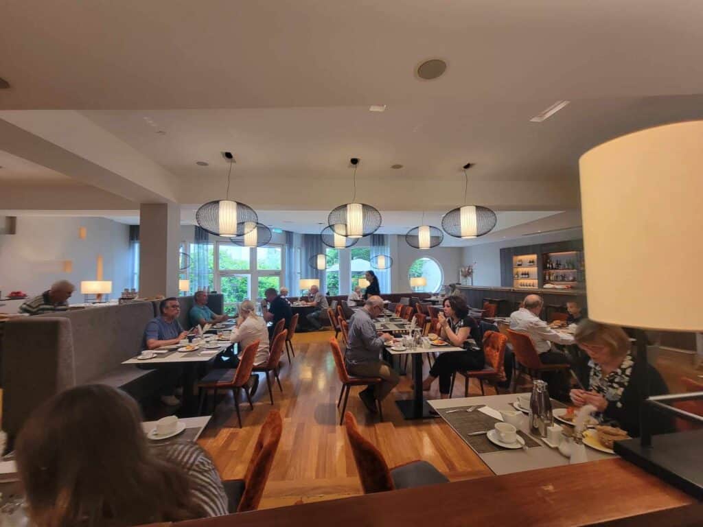 A full dining room with wooden floor and modern light fixtures and daylight out the large windows in the back